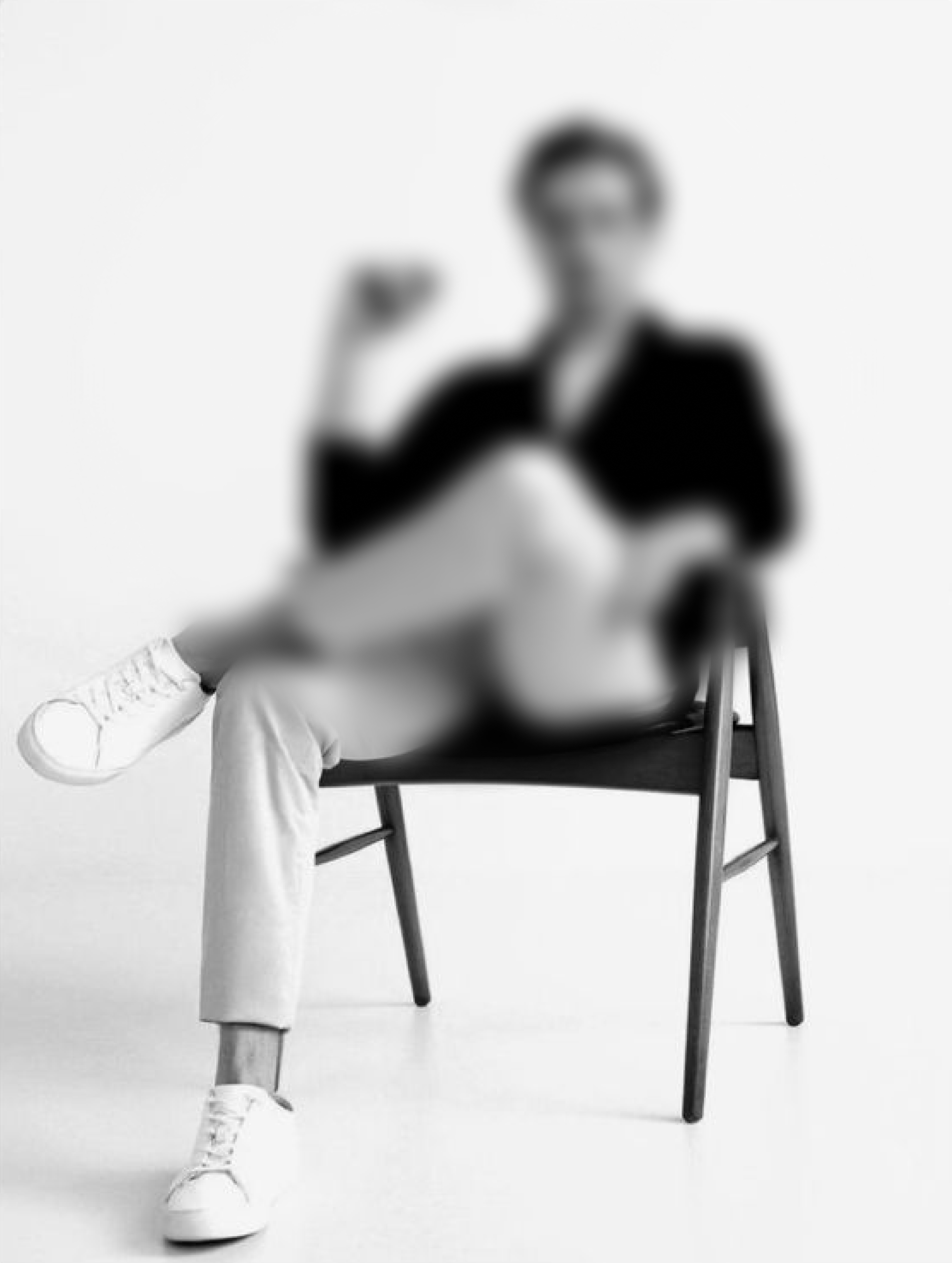 A man sitting on a chair, wearing black jacket, white pants and white sneakers